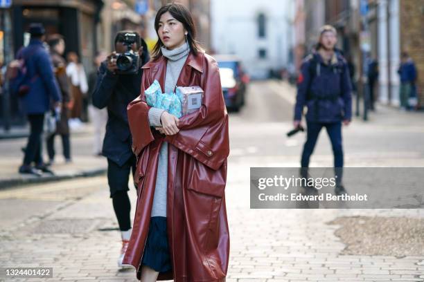 Guest wears silver earrings, a pale gray ribbed wool turtleneck long pullover, a long oversized red leather puffy sleeves coat, a black pleated long...