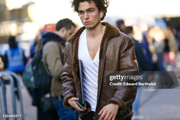 Guest wears a white t-shirt, a brown leather sheep collar bomber jacket, black pants, a black shiny leather clutch, during London Fashion Week Men's...