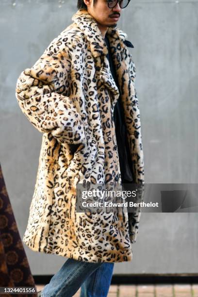 Guest wears glasses, a beige and brown leopard pattern long fluffy coat, blue denim jean pants, a black pullover, during London Fashion Week Men's...