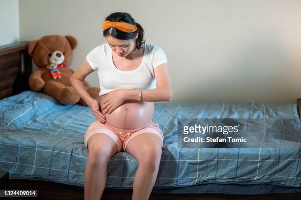 mujer embarazada aplicando aceite corporal hidratante en su vientre en el dormitorio - estrias fotografías e imágenes de stock