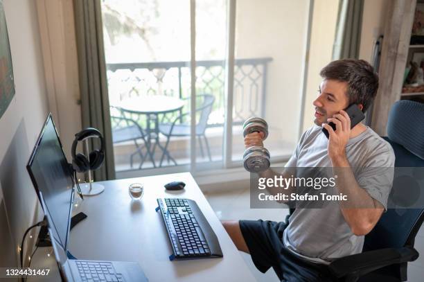 man exercising to stay in shape while working from home in an improvised office in the living room - lifehack stockfoto's en -beelden