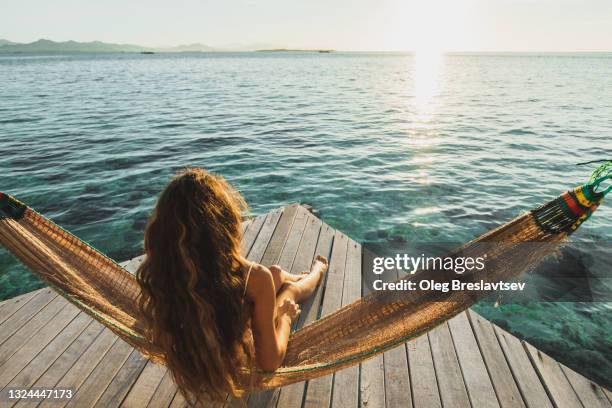 view from behind of woman awakening with ocean view.  wooden hotel terrace with hammock. beautiful morning light - descanso fotografías e imágenes de stock