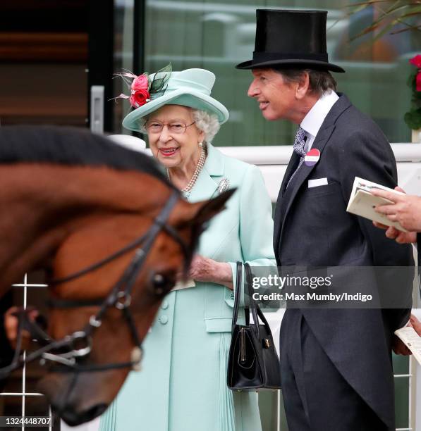 Queen Elizabeth II, accompanied by her racing manager John Warren, holds a racecard as she stands in the parade ring on day 5 of Royal Ascot at Ascot...