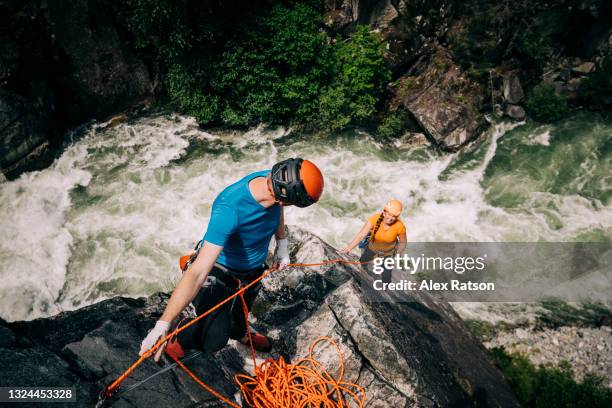 male rock climber belays female climber up a rock climb high above a canyon near whistler, bc - free falling stock pictures, royalty-free photos & images