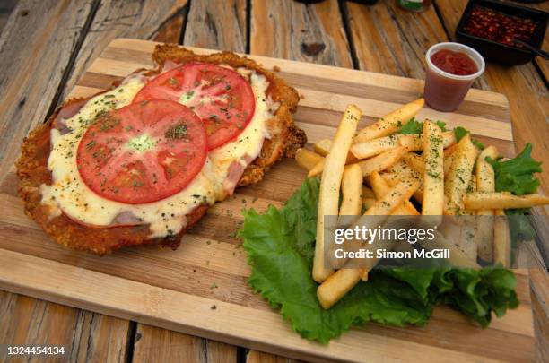 milanesa a la napolitana (thin slice of fried beef filet topped with tomato sauce, ham, mozzarella cheese and fresh tomato slices) on a wooden cutting board with fries and ketchup - milanese stockfoto's en -beelden