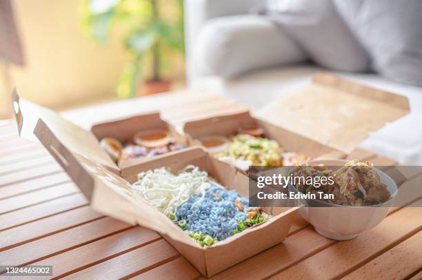 malaysische lebensmittel nasi kerabu, nasi ulam und ayam percik in recycling-papier-behälter mit sauce auf couchtisch neben sofa im wohnzimmer - calamansi stock-fotos und bilder