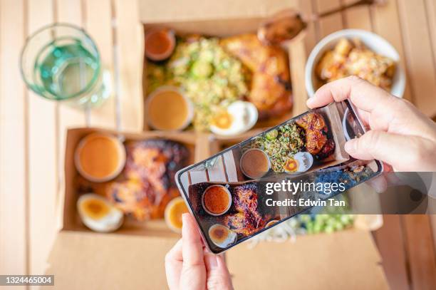 personal perspective human hand taking photo using smart phone on table top view malaysian food nasi kerabu, nasi ulam and ayam percik in recycled paper container with sauce - estilismo culinário imagens e fotografias de stock