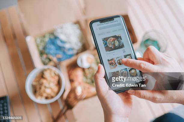high angle view close up asian woman using meal delivery service ordering food online with mobile app on smartphone in the living room at a cozy home - applicatie stockfoto's en -beelden