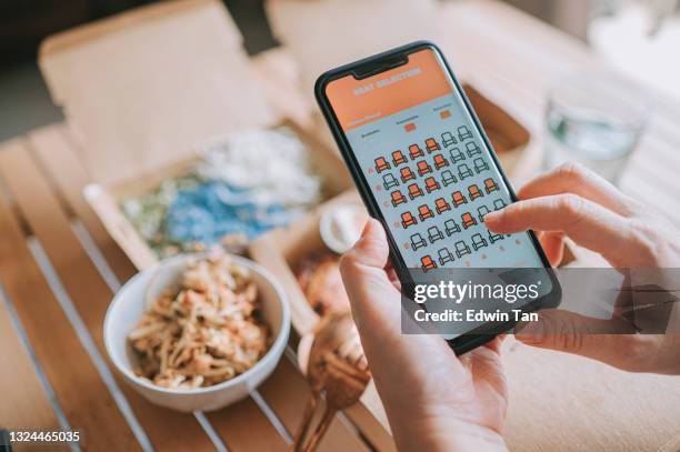 high angle view close up asian woman using mobile app cinema movie e-ticketing reservation on smartphone in front of take out food at home - and booking com application stock pictures, royalty-free photos & images