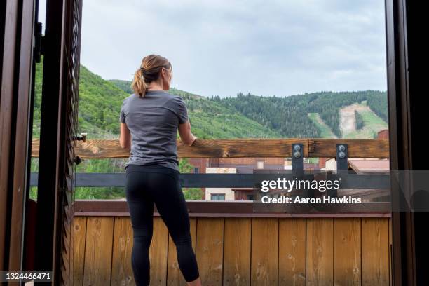 athletic fit woman admiring the view from the balcony of her hotel room near a mountain ski resort - female skier stockfoto's en -beelden