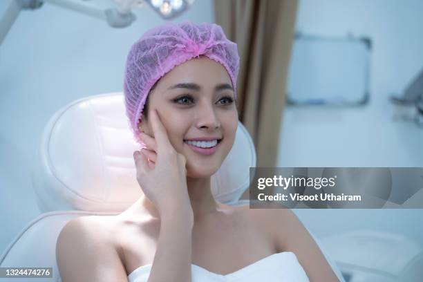 portrait of  young female client in a beauty clinic white turban sits on the bed checking the beauty of her face. - laser face stock pictures, royalty-free photos & images