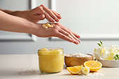 Woman applying body scrub on hand at wooden table, closeup