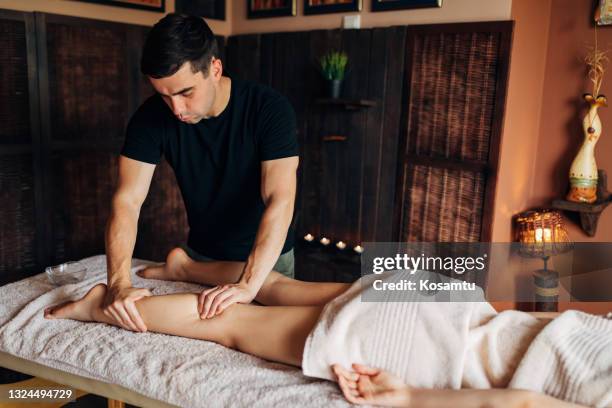 giovane donna che si gode il massaggio terapeutico al polpaccio dal massaggiatore maschile professionista - woman lying on stomach with feet up foto e immagini stock