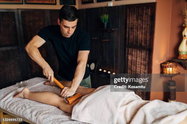 massagista usando o rolo de bambu enquanto realizava a massagem anti-celulite nas coxas da cliente feminina - celulite aspecto da epiderme - fotografias e filmes do acervo