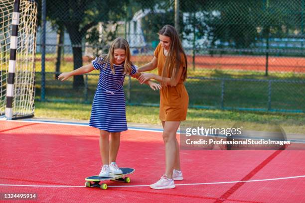 young mother is having fun with her daughter while they riding a skateboard together. - mother and daughter riding on skateboard in park stock pictures, royalty-free photos & images