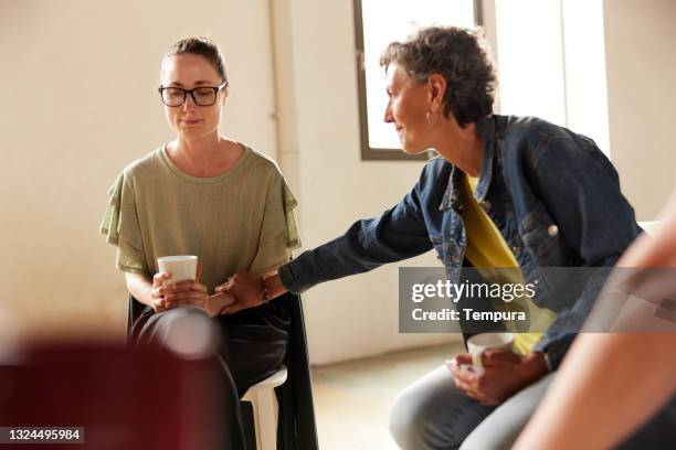 a woman in group therapy gives support to another member. - empathy stockfoto's en -beelden