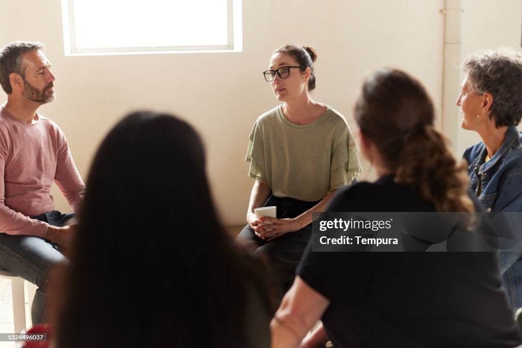 A sad woman is talking to the other members of the therapy group.