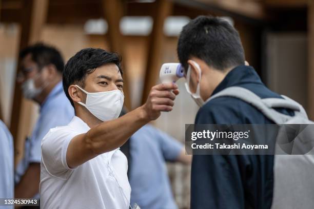 An employee checks the body temperature of a man during press preview of the Village Plaza as part of the Olympic and Paralympic Village media tour...