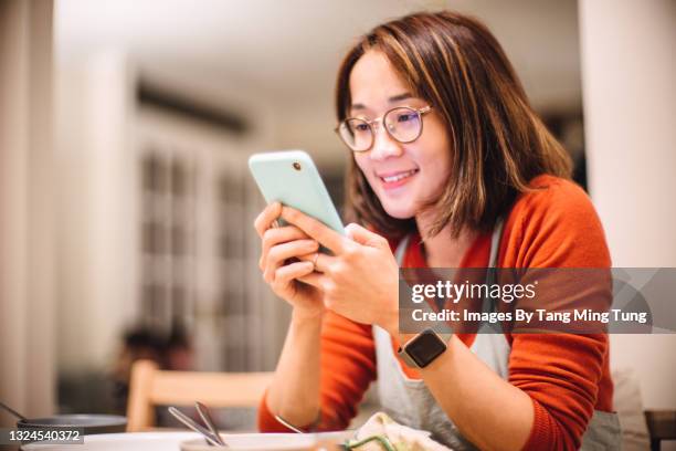 young pretty woman using smartphone joyfully at home - madre ama de casa fotografías e imágenes de stock