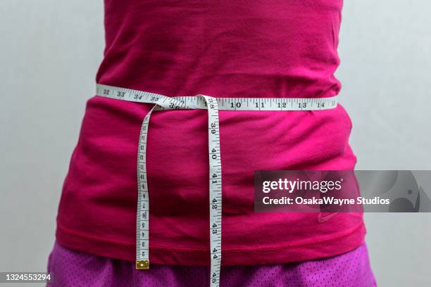 close-up of adult slim woman in pink sportswear with inch scale measuring tape around waist. - waistband 個照片及圖片檔