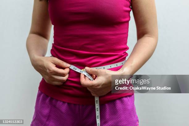 midsection of adult slim woman in sportswear measuring waist circumference. inch scale of measuring tape. - waist stockfoto's en -beelden
