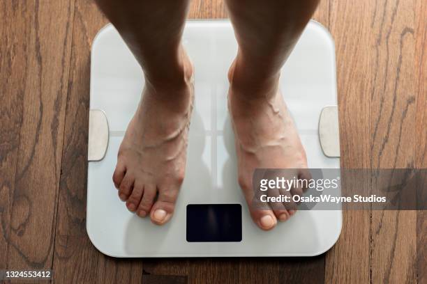 top down view of feet standing on white digital bathroom scale over wooden floor. - weight scale stock-fotos und bilder
