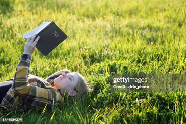 young girl reading bible in the meadow - bible stock pictures, royalty-free photos & images