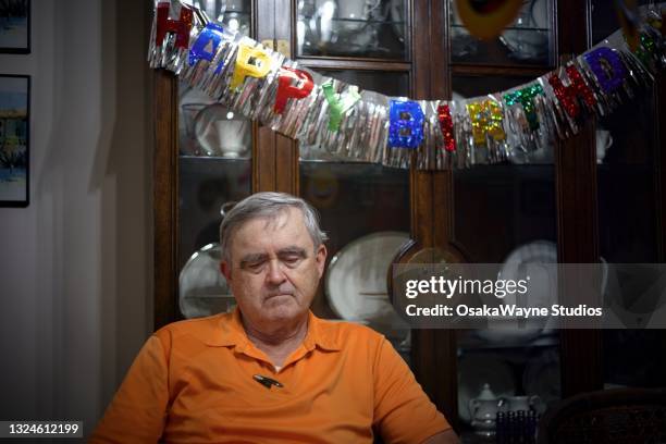 sad old man in front of "happy birthday" banner. - sad birthday stock pictures, royalty-free photos & images