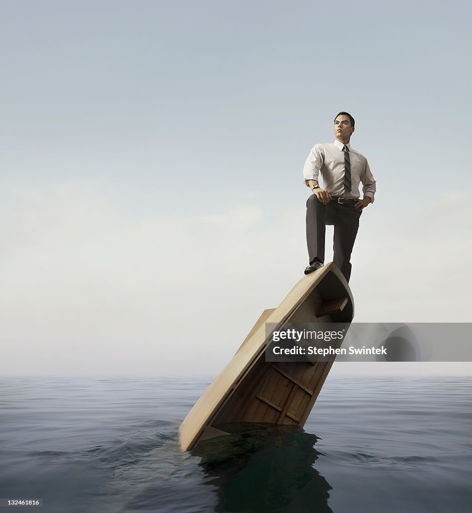 Businessman standing atop a sinking boat