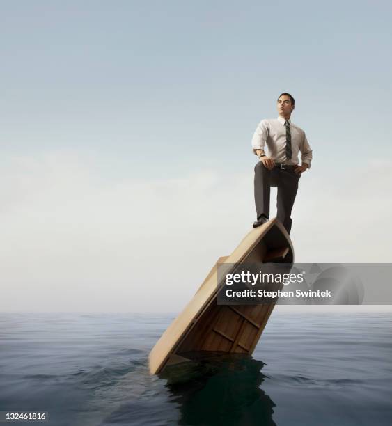 businessman standing atop a sinking boat - sinking foto e immagini stock