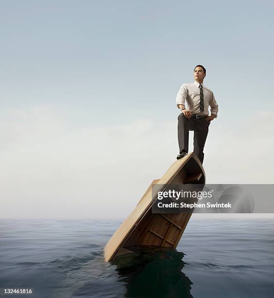 businessman standing atop a sinking boat - sinking stockfoto's en -beelden