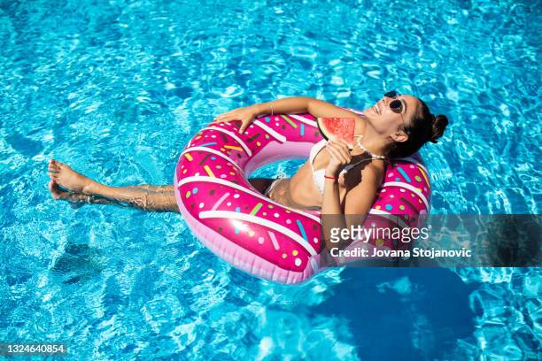 beautiful, attractive woman enjoys the pool in an inflatable donut and holds watermelons - buitenbad stockfoto's en -beelden