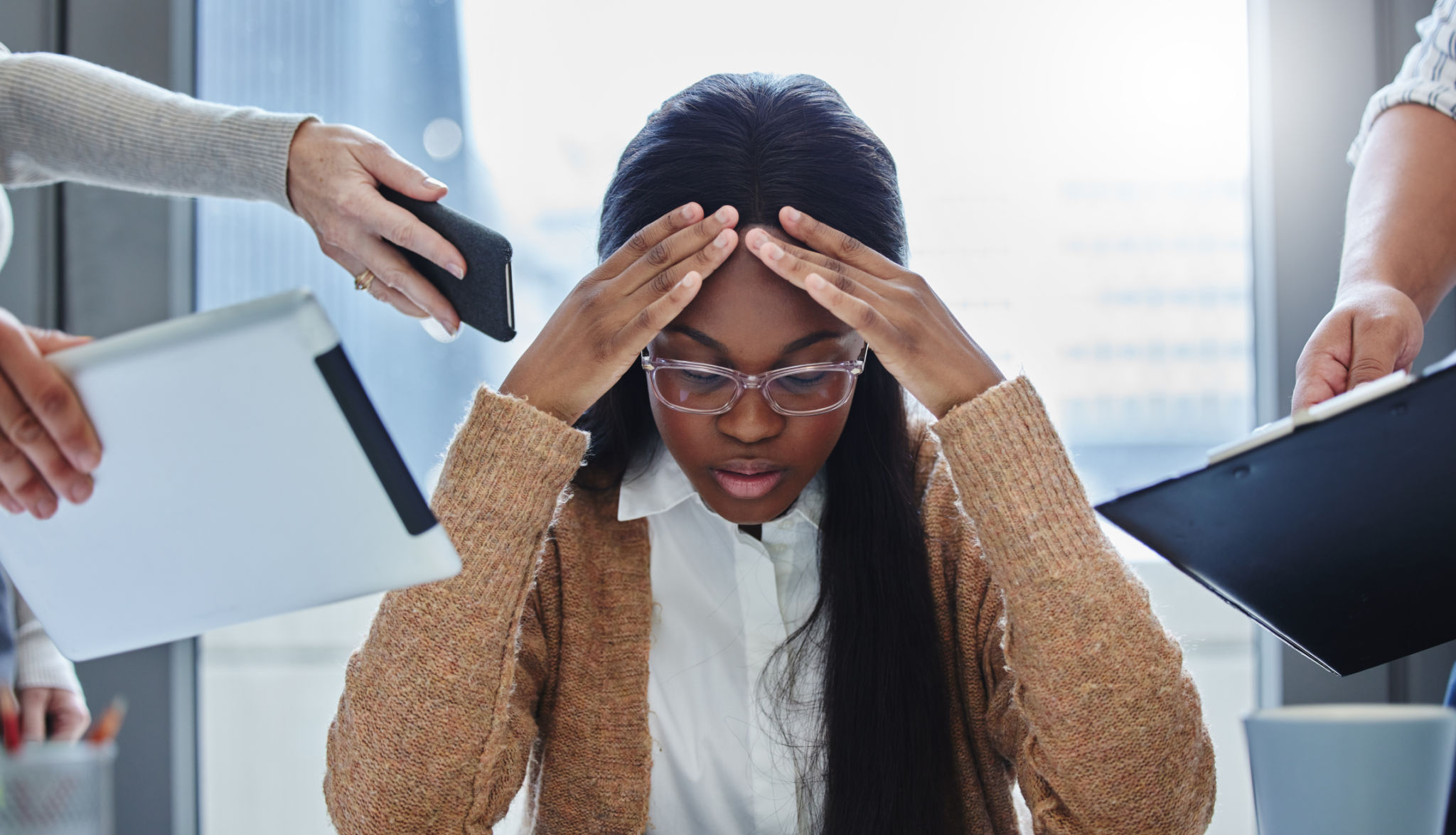 Shot of a young businesswoman sitting in the office and feeling stressed while colleagues overwhelm her with tasks Shot of a young businesswoman sitting in the office and feeling stressed while colleagues overwhelm her with tasks