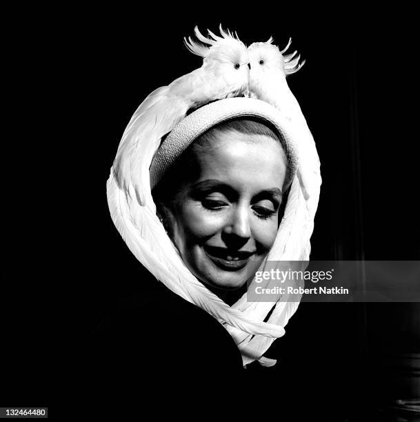 Woman smiles while modeling a hat adorned with a bird motif, created by Ben Bess Hats, Chicago, 1950. The hat comes in the shape of two birds facing...