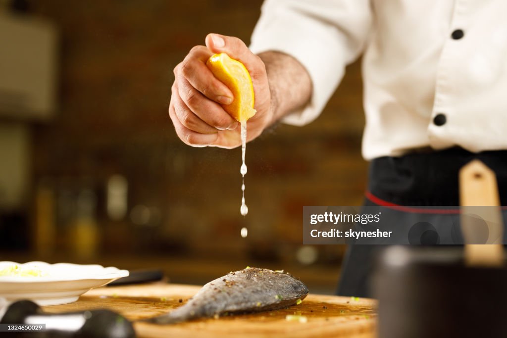 Close up of unrecognizable chef squeezing lemon juice on fish.