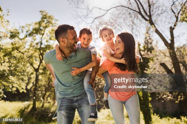 happy parents having fun while piggybacking their small kids in nature. - springtime stockfoto's en -beelden