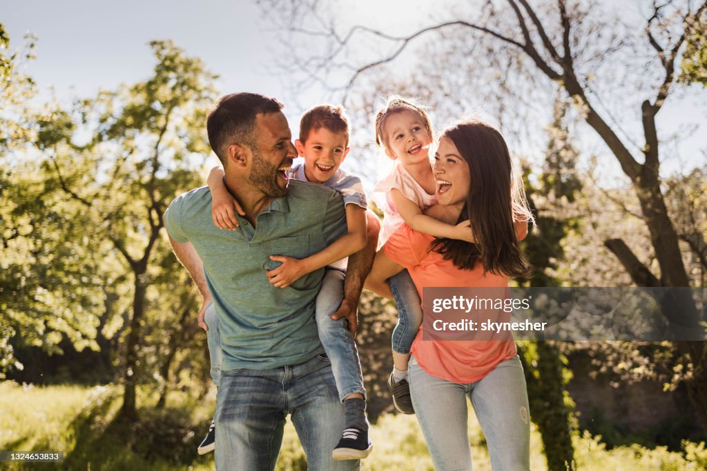 Happy parents having fun while piggybacking their small kids in nature.