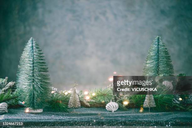 christmas background with christmas trees, fir green, pine cones and lights on table with festive table cloth at wall background - christmas background green stock-fotos und bilder