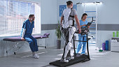 Male and female therapists controlling rehabilitation of man in exoskeleton