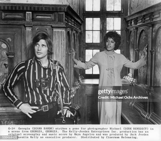 Dirk Benedict stands as Diana Sands strikes a pose for photographer in a scene from the film 'Georgia, Georgia', 1972.