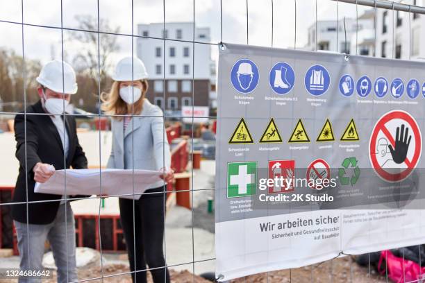 un tablero de advertencia adjunto a la cerca del sitio en un sitio de construcción. en el fondo, un arquitecto o ingeniero civil está hablando con una mujer - conceptos y temas fotografías e imágenes de stock