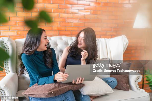 two young asian female women friends sharing happy time together ,two friend relax with laptop on sofa living room - luxury girl stock pictures, royalty-free photos & images