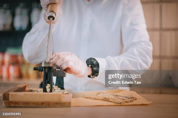 asiatische chinesische männliche apotheker schneiden ginseng chinesische kräuter medizin in traditionellen chinesischen kräutermedizin shop - ginseng stock-fotos und bilder