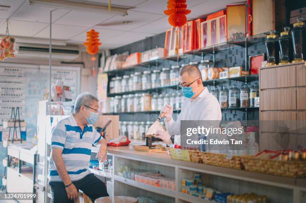 pharmacien masculin chinois asiatique coupant la médecine aux herbes chinoises de ginseng pour son patient senior à la boutique de phytothérapie traditionnelle chinoise - médecine chinoise par les plantes photos et images de collection