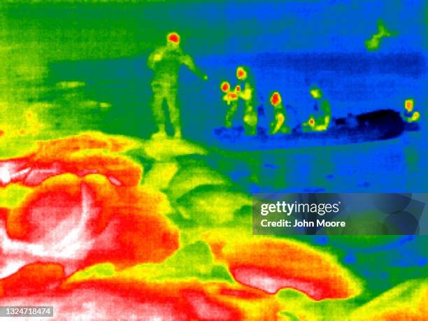 In this image made with a thermal camera, A Texas National Guard soldier assists a child onto the bank of the Rio Grande at night on June 19, 2021 in...