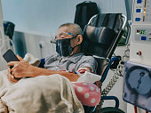 asian chinese senior man in wheelchair with face shield , face mask under dialysis treatment in hospital using smart phone