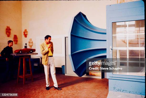 View of American film director John Frankenheimer smokes a pipe as he looks into a wind tunnel at the Ferrari automobile factory, Maranello, Italy,...