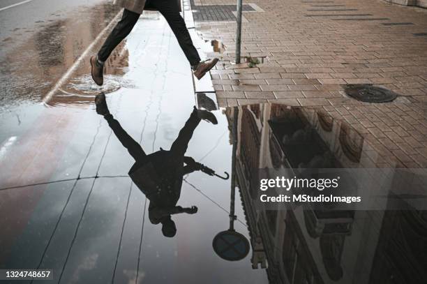 section basse d’un homme marchant dans la rue humide avec réflexion dans l’eau - chaussures couleur or photos et images de collection