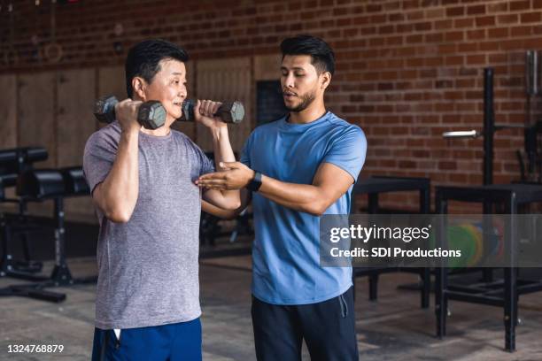personal trainer helps senior man with weights - instrutor de fitness imagens e fotografias de stock