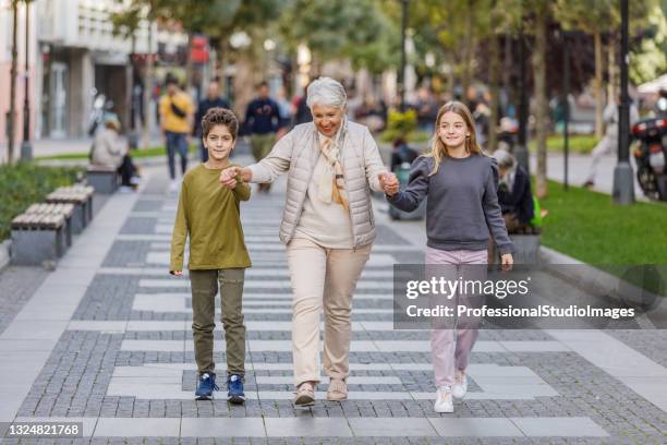 an elderly woman is walking in the city streets with her grandson and granddaughter. - ageing population stock pictures, royalty-free photos & images